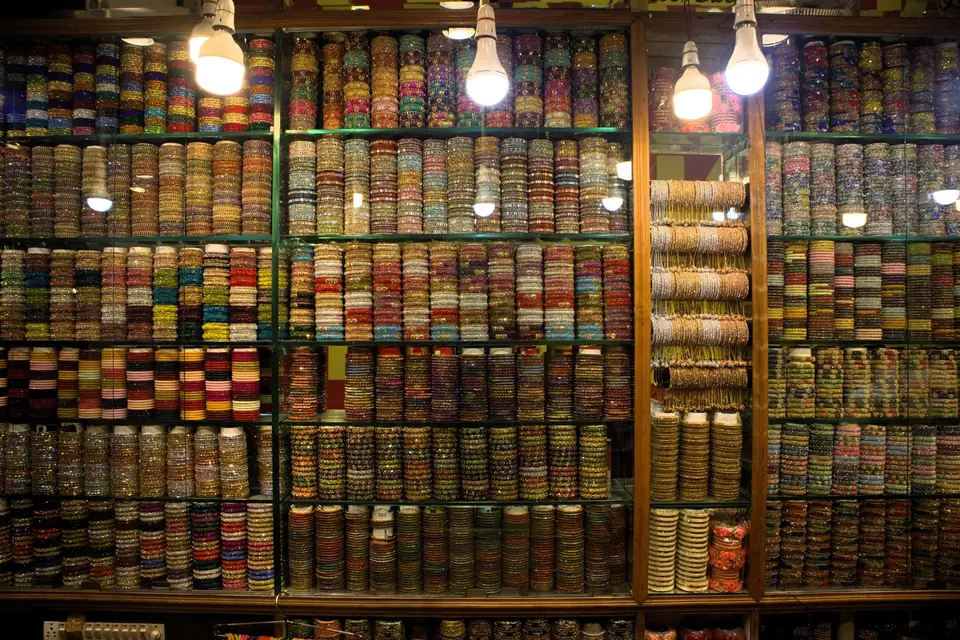 Glass-fronted shop shelves packed with stacks of colourful bangles under bare light bulbs