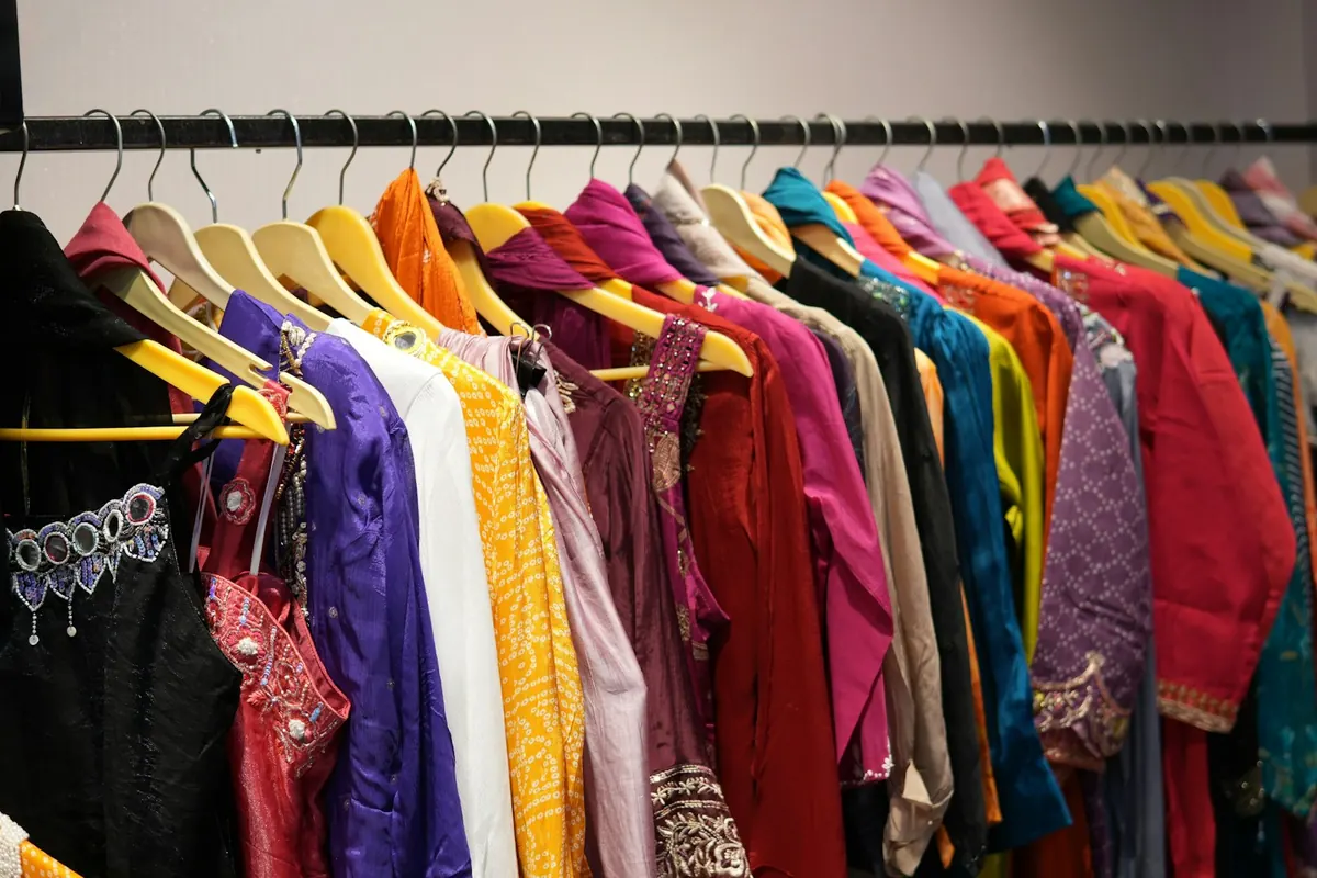 Colourful kurtis and tops with embroidered necklines hanging from yellow hangers along a black clothing rail