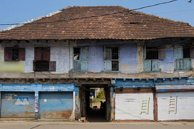An old two-storey building in Kochi with a tiled roof and closed blue and white roller shutters at street level.