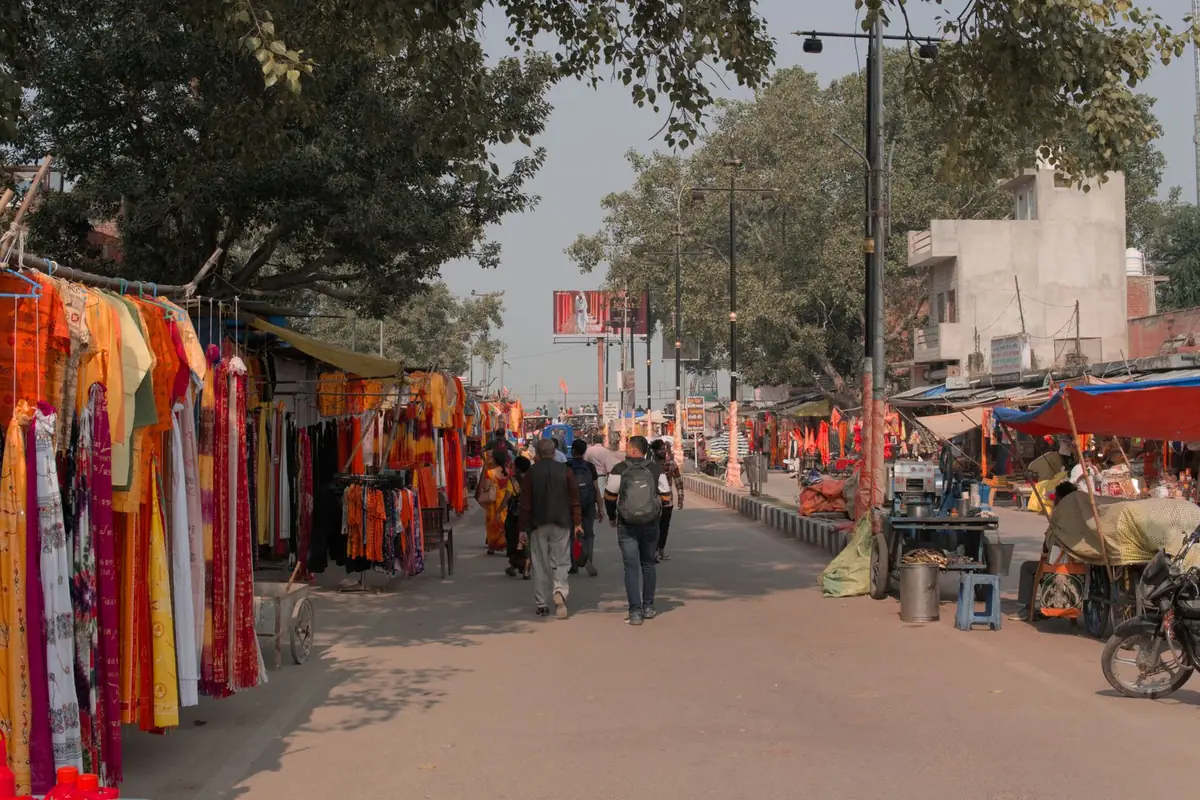A street market in Ayodhya with clothes hanging on racks on the left, stalls on the right and a few people walking away down the road.